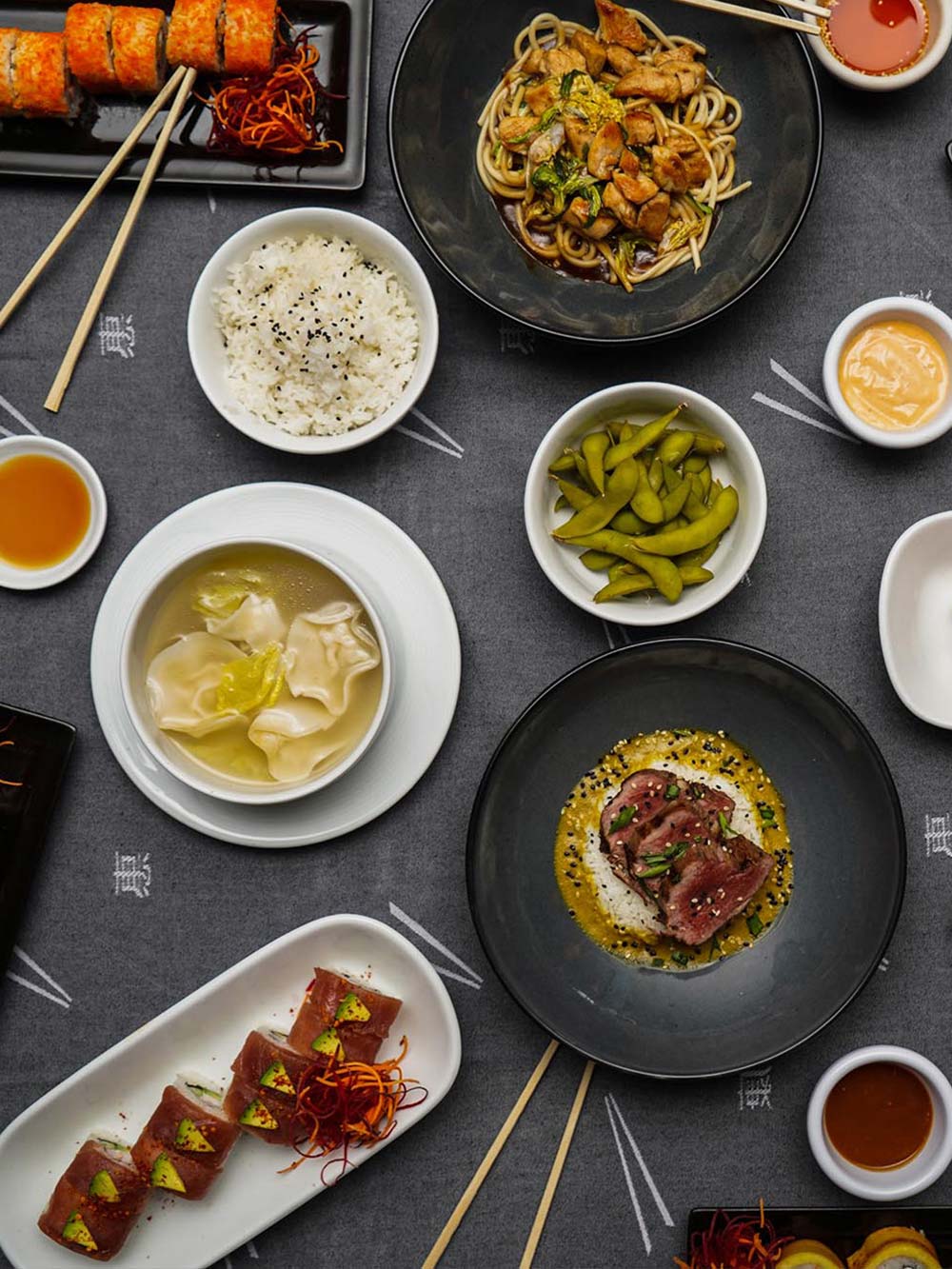 Black table with an array of sushi and veggie dishes